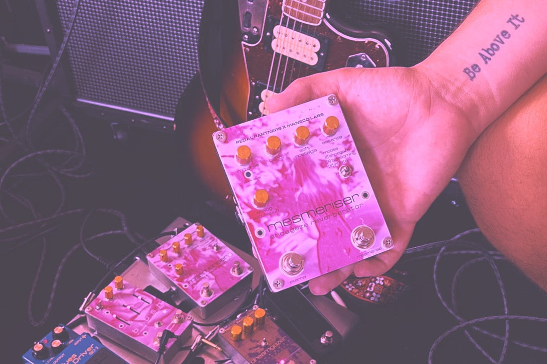 guitarist holding mesmeriser reverb pedal in front of guitar and pedalboard of guitar pedals
